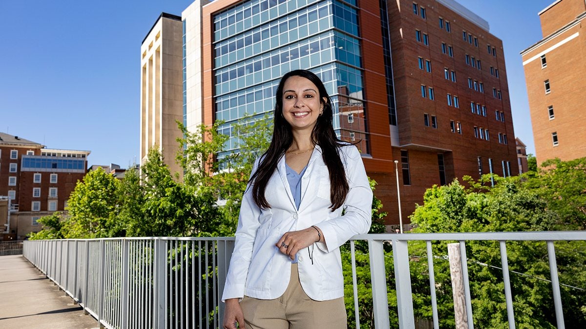 Supriya Caton posing for photo on bridge on the campus of UNC-Chapel Hill with medical buildings seen in the background