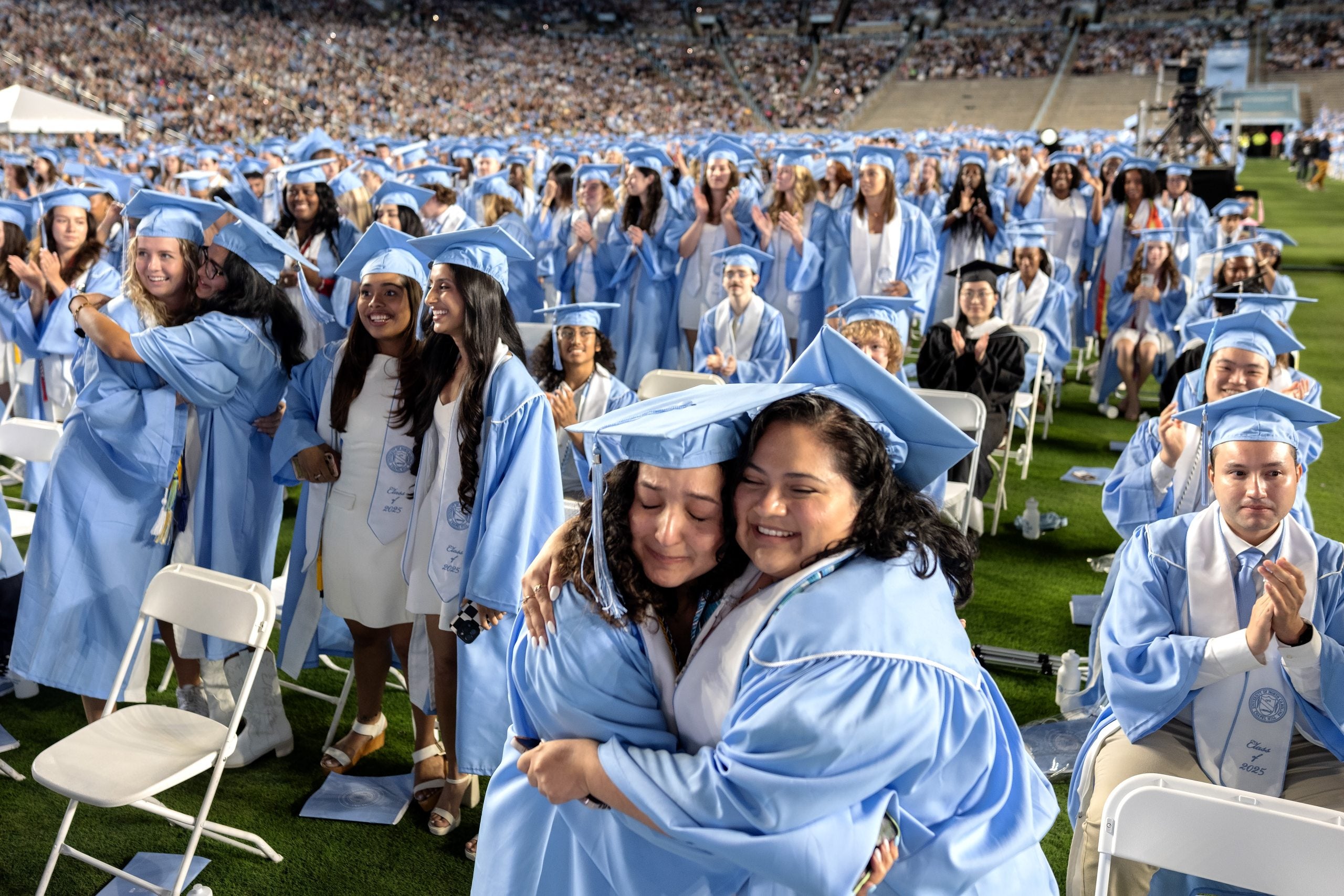 Graduates hug on the field at Spring Commencement