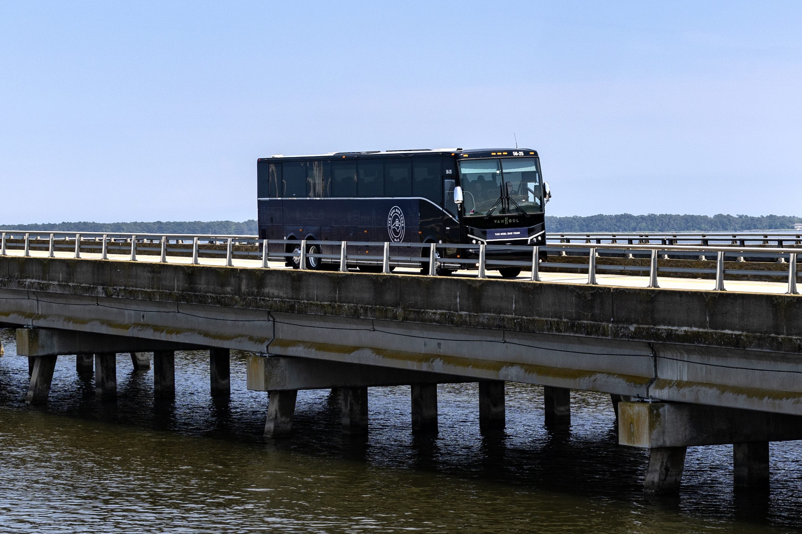 Navy blue Tar Heel Bus Tour bus driving over a bridge over a waterway.