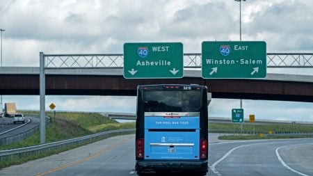 Carolina Blue Tar Heel Bus Tour bus driving on the highway and approaching signs for Asheville and Winston-Salem.