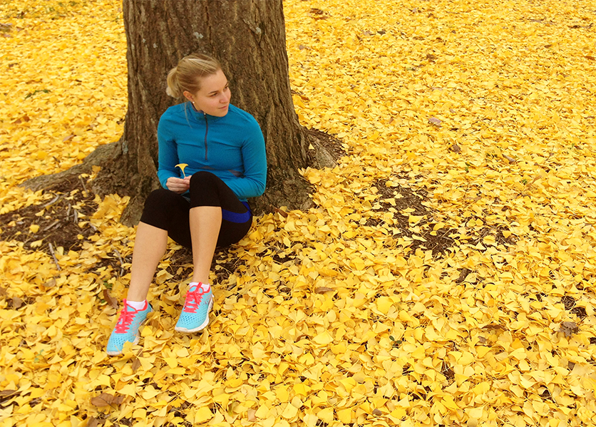 A female student sits under the ginkgo tree with vibrant yellow leaves on the ground.