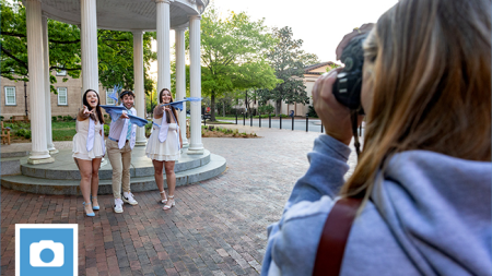 Photographer Samantha Lewis making a photo of Brittany Harrelson, Nick Clementi, and Shaena Riddles getting ready to toss their graduation caps in front of the Old Well on the campus of UNC-Chapel Hill.