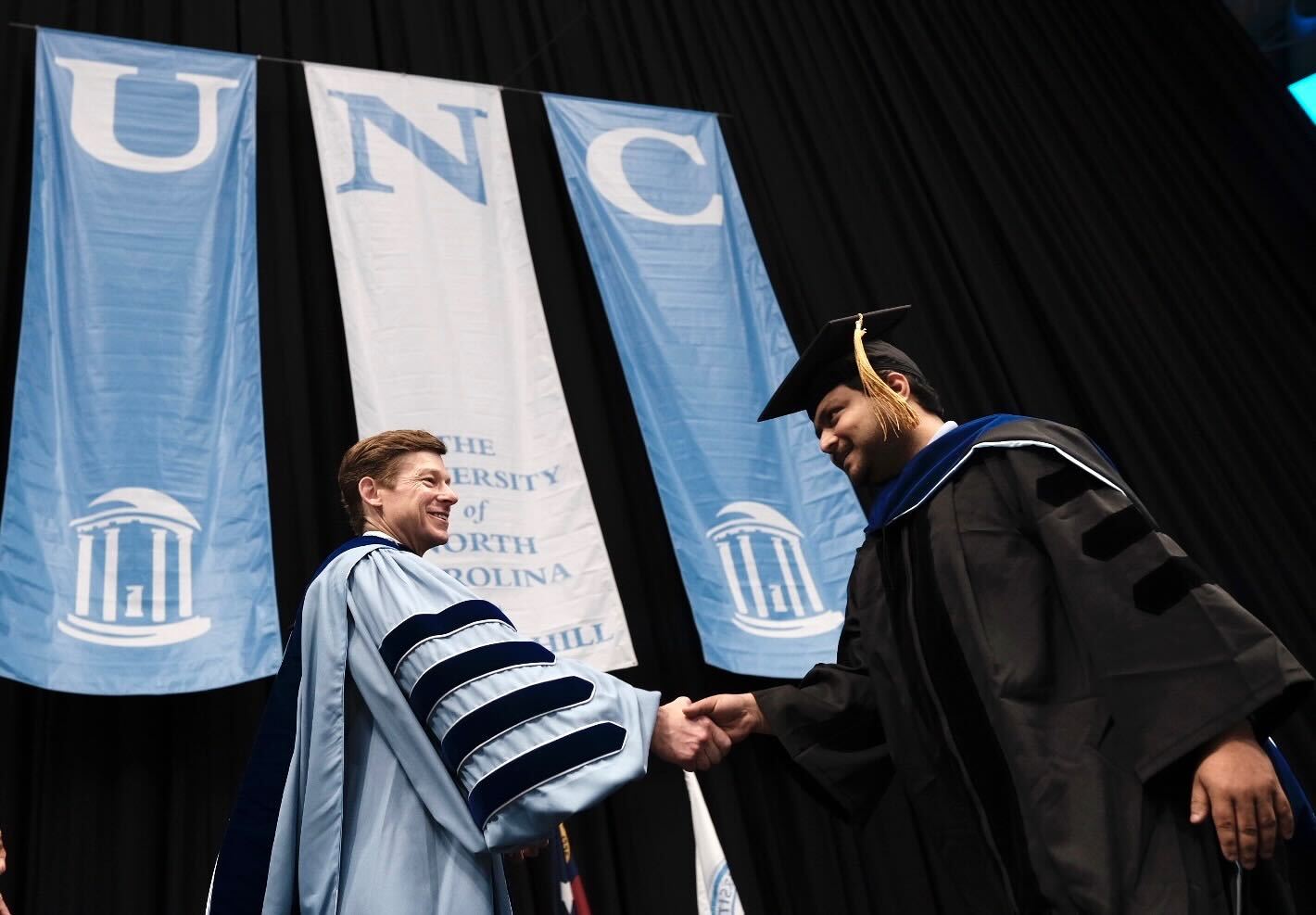 Chancellor Lee H. Roberts shakes a graduate student's hand on stage during the Doctoral Hooding ceremony.