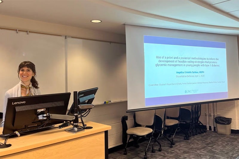 Woman smiling at a podium in front of a presentation title slide.