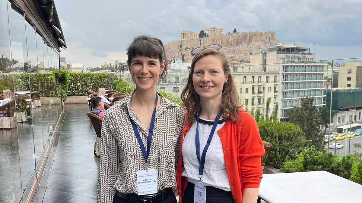 Two women smiling with the city of Athens, Greece and the Acropolis in the background.