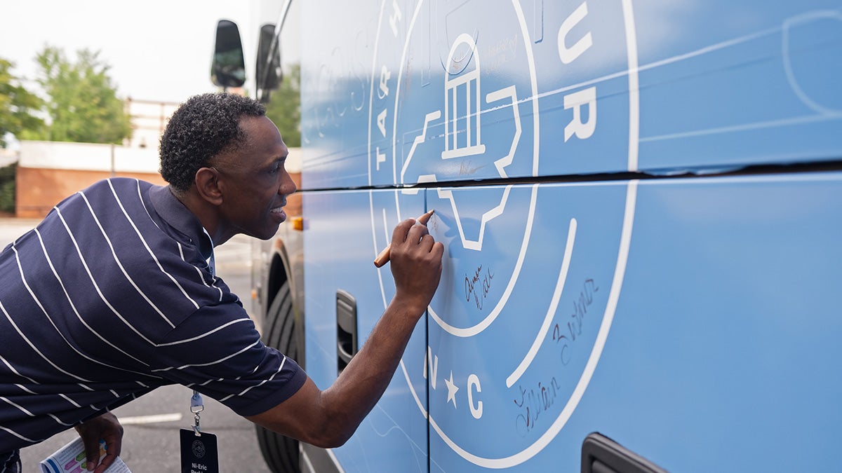 Ni-Eric Perkins, a Tar Heel Bus Tour participant, writes his name on the bus