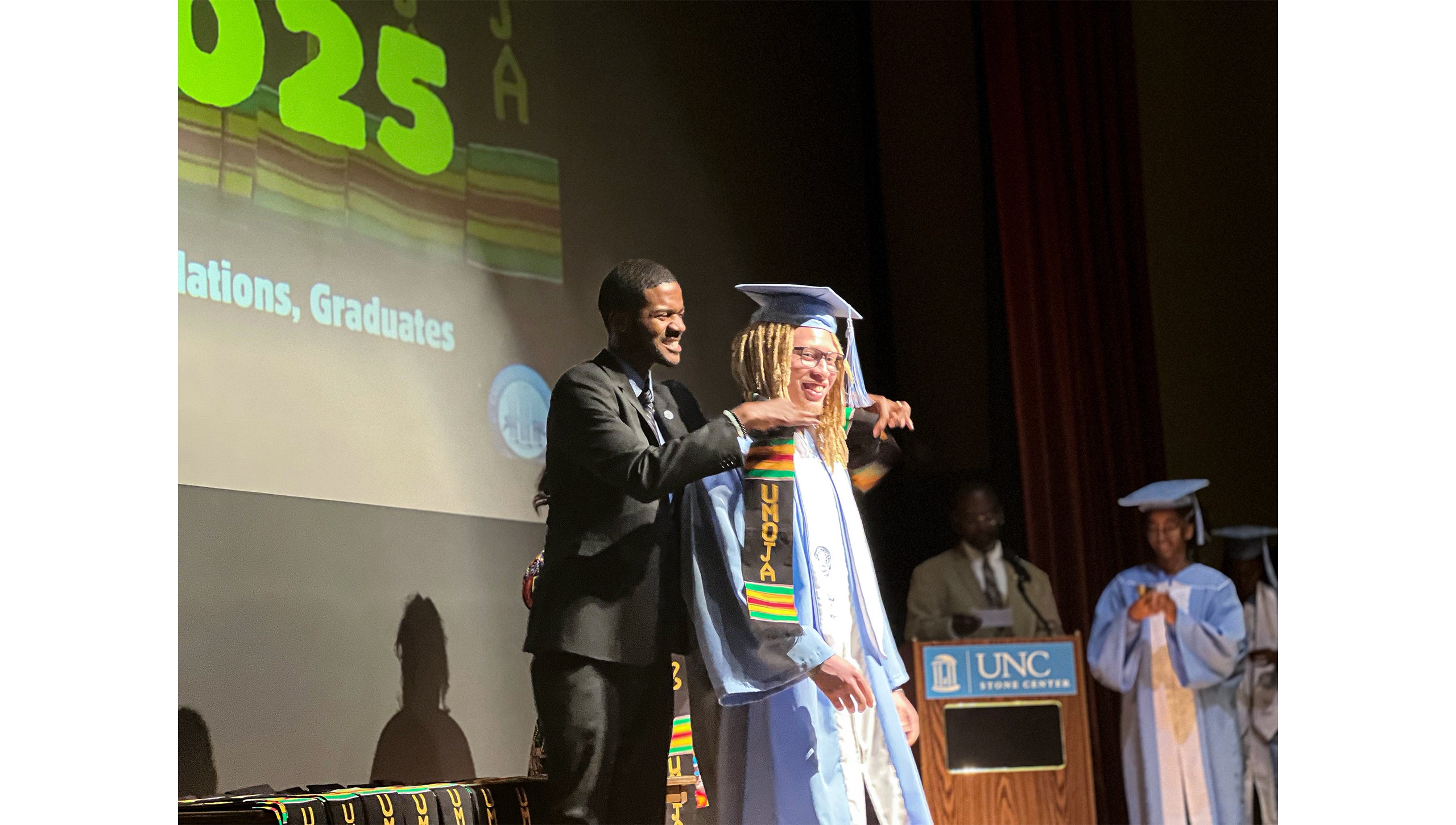 A graduate is recognized on stage at Umoja Graduation