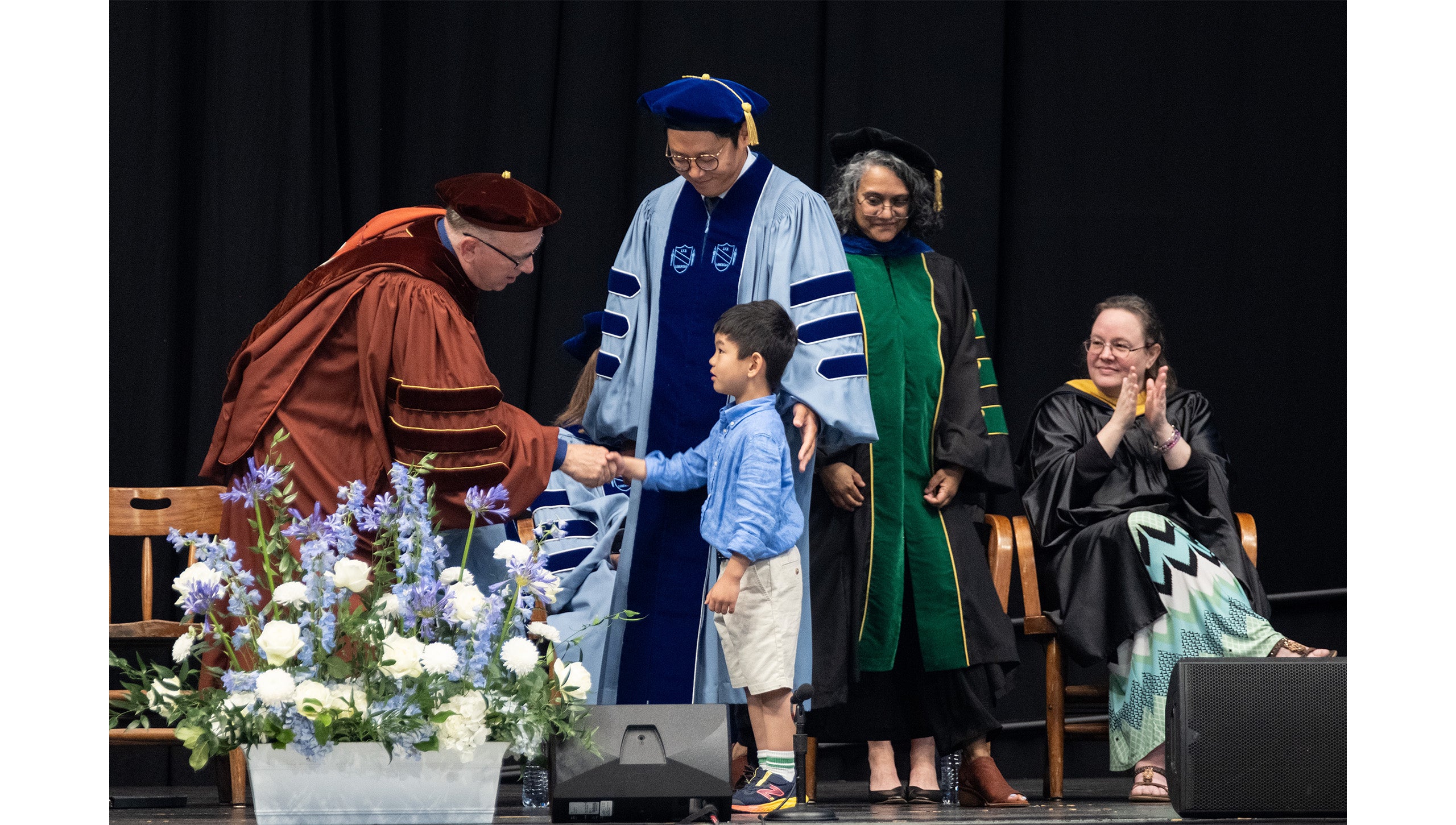 A doctoral graduate's son shakes hands with Provost Chris Clemens during the 2025 Doctoral Hooding Ceremony