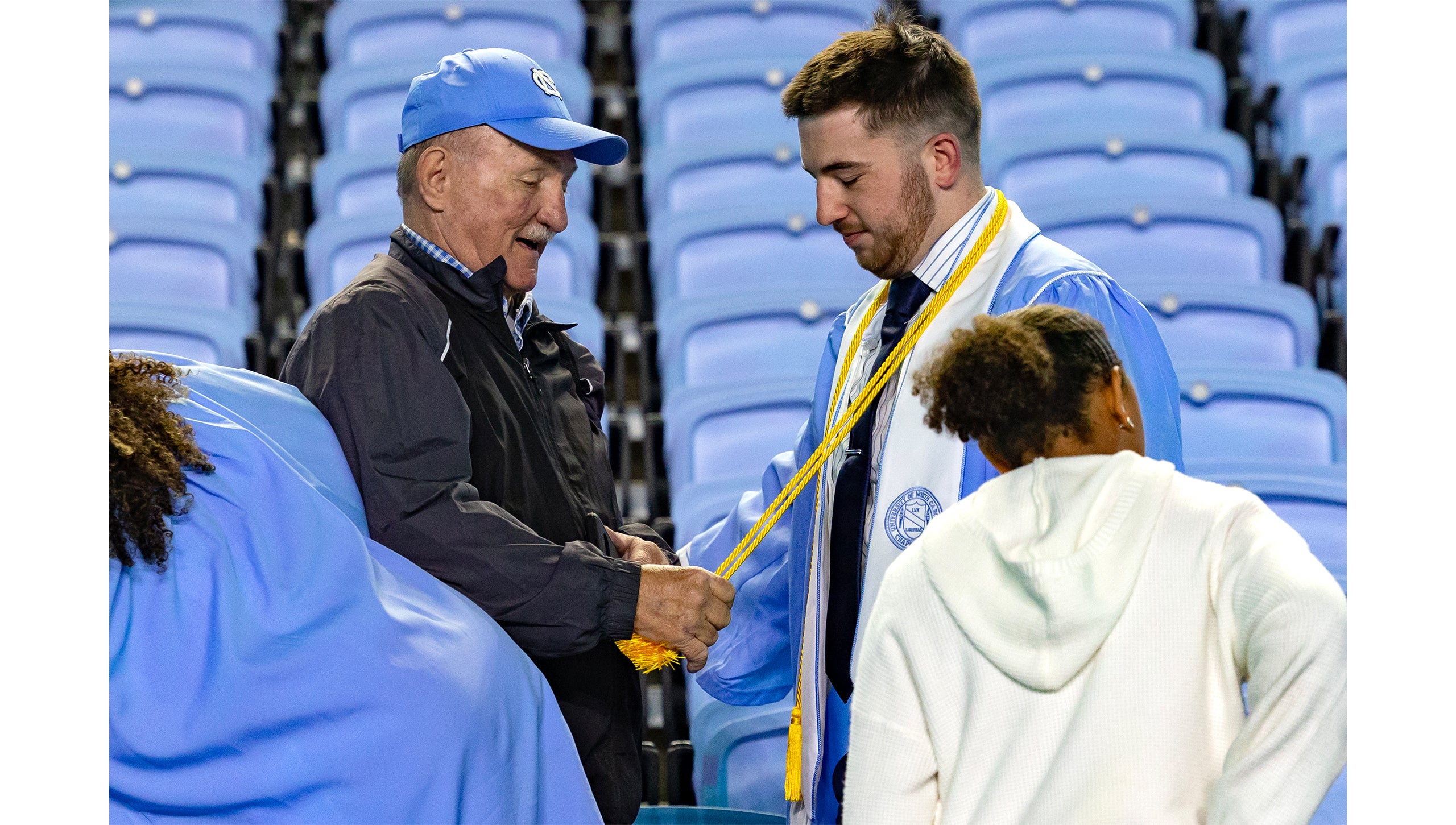 A graduate's family member tugs on their graduation cords after Spring Commencement 2025.