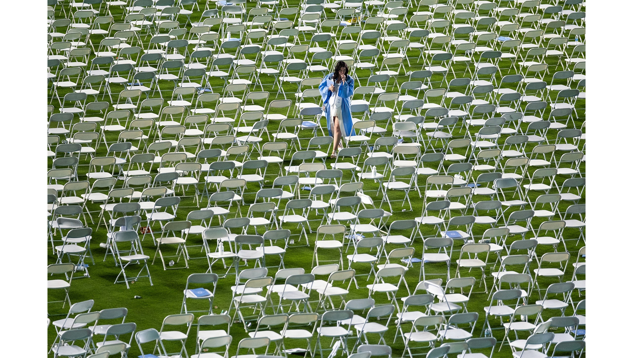 A graduate walks amid a sea of empty chairs after Carolina's Spring Commencement.
