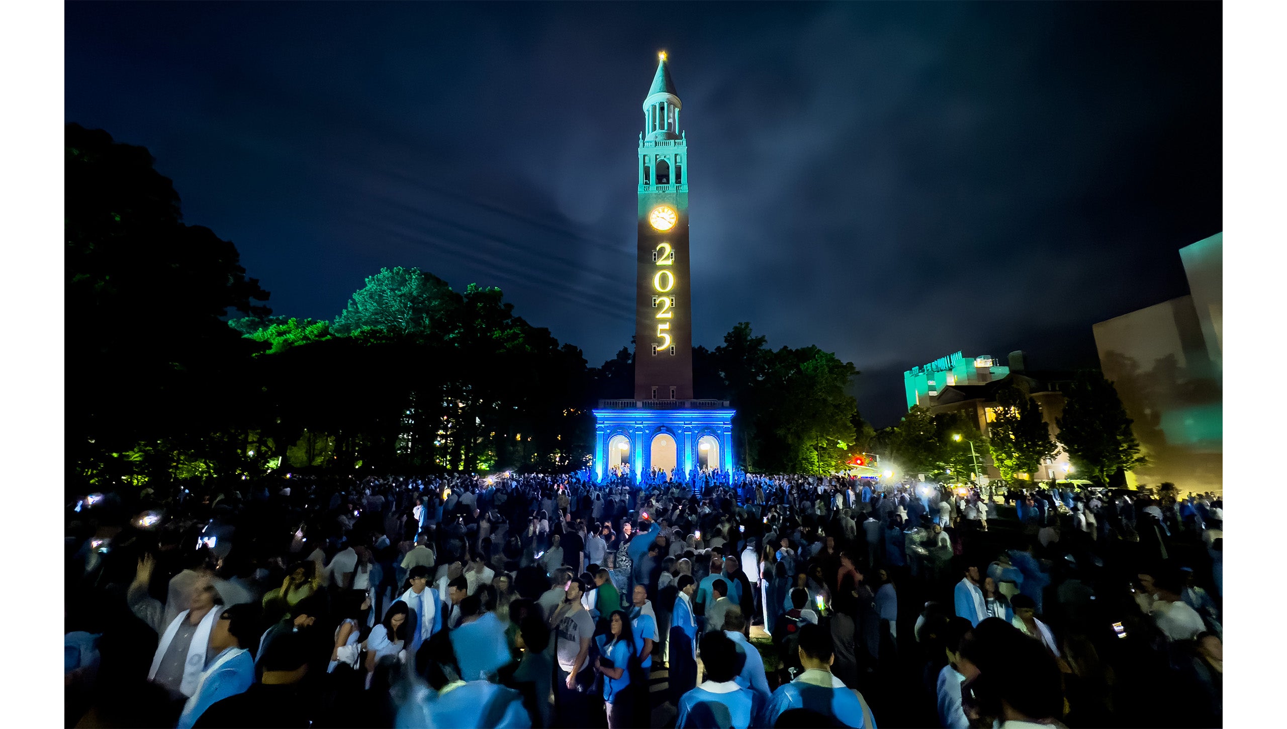 Graduates and their families gather around the Bell Tower, illuminated with 