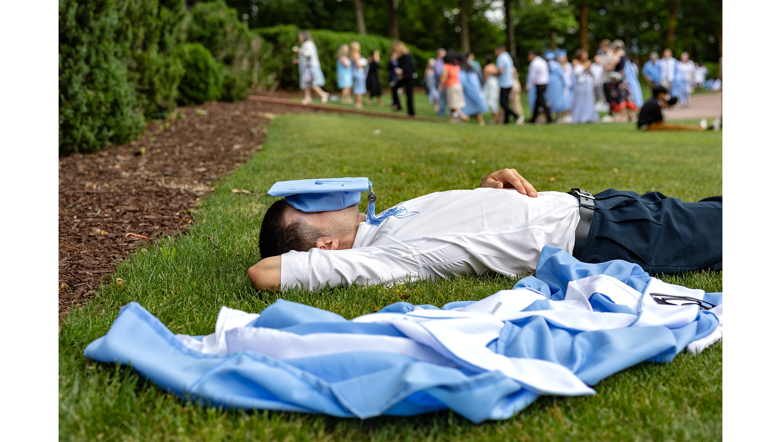A graduate lies on the ground with his cap on his head before Spring Commencement.