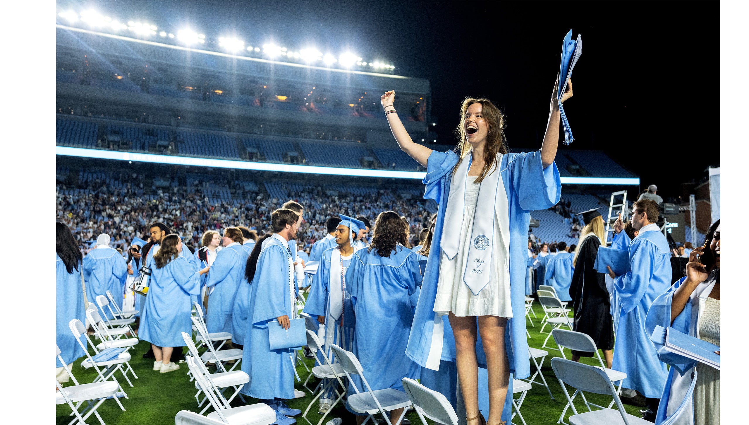 A graduate stands on her chair to cheer during Carolina's 2025 Spring Commencement.