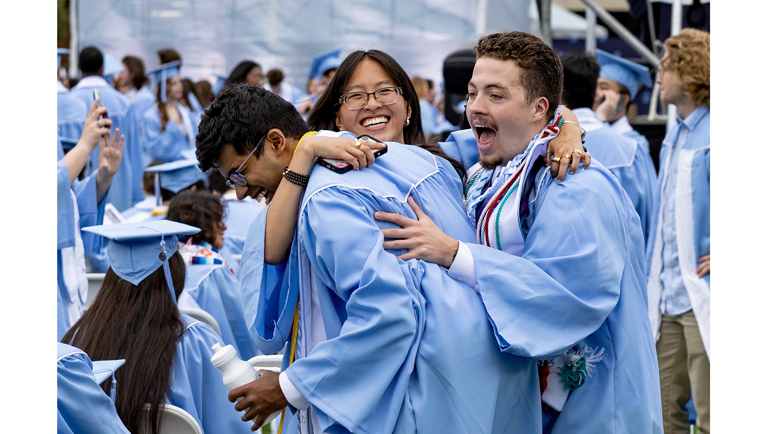 Graduates hug on the field before Spring Commencement.