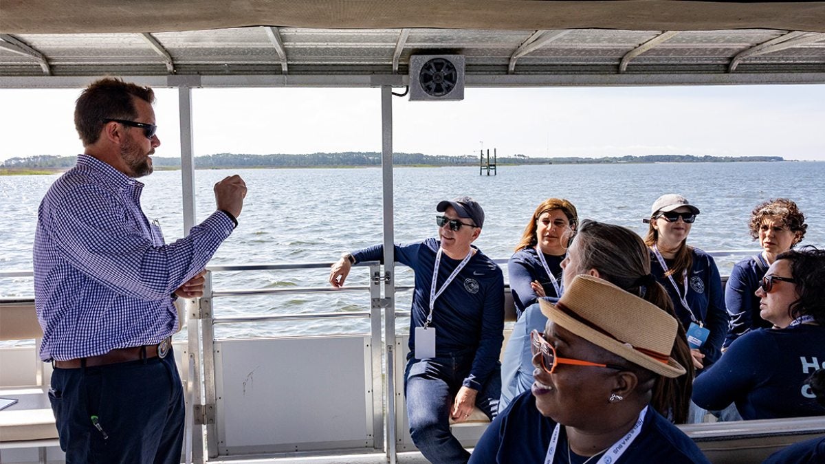 A man speaking to Tar Heel Bus Tour attendees aboard a boat.