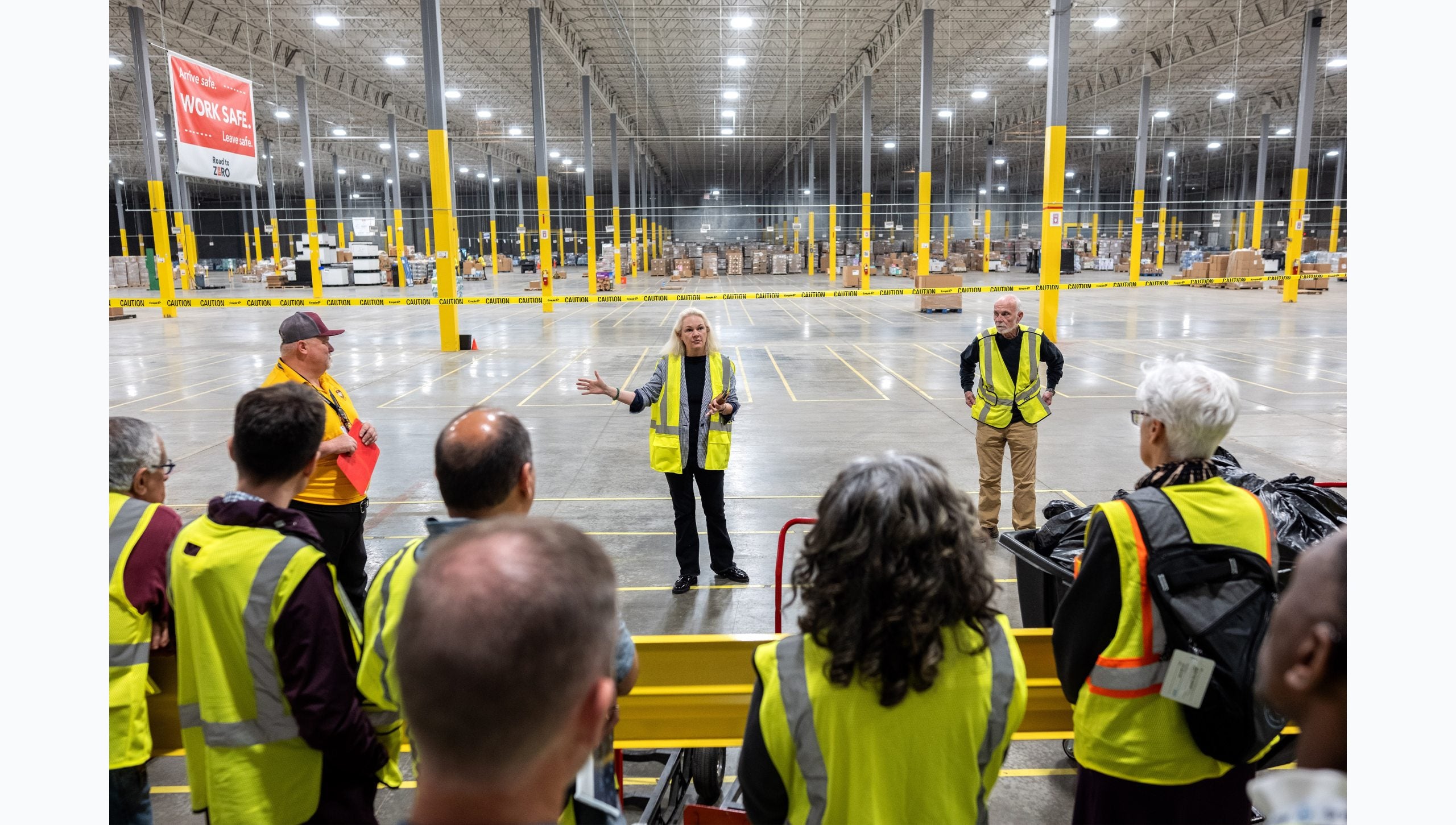 Tar Heel Bus Tour participants listening to workers speak in a large supply warehouse.