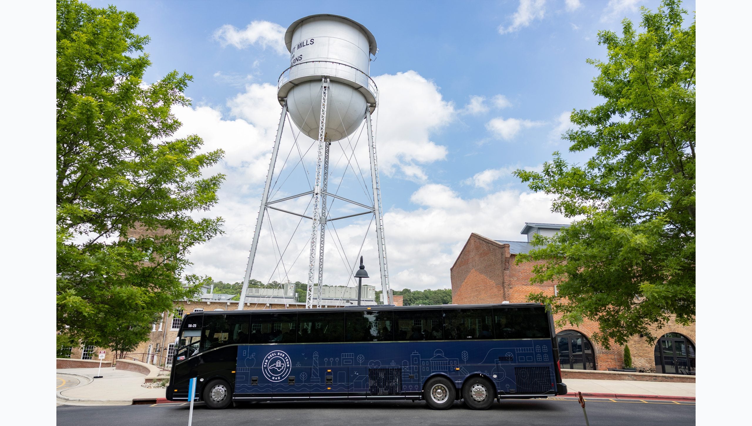 Navy blue West route bus driving by Rocky Mount Mills.