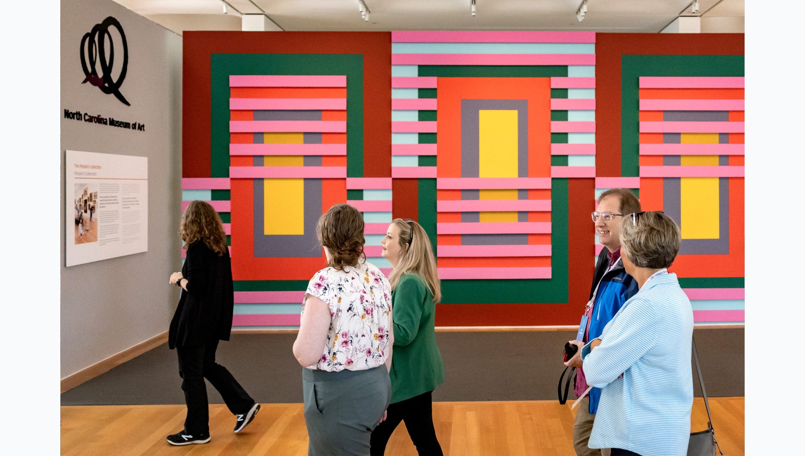 Tar Heel Bus Tour participants walking by vibrant and wall-wide art at the North Carolina Museum of Art.