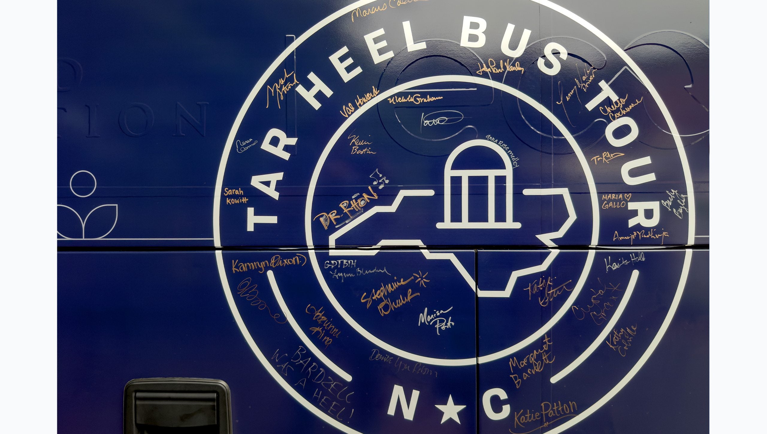 Tar Heel Bus Tour logo with signature of attendees on and around the logo on the side of the Navy blue bus.