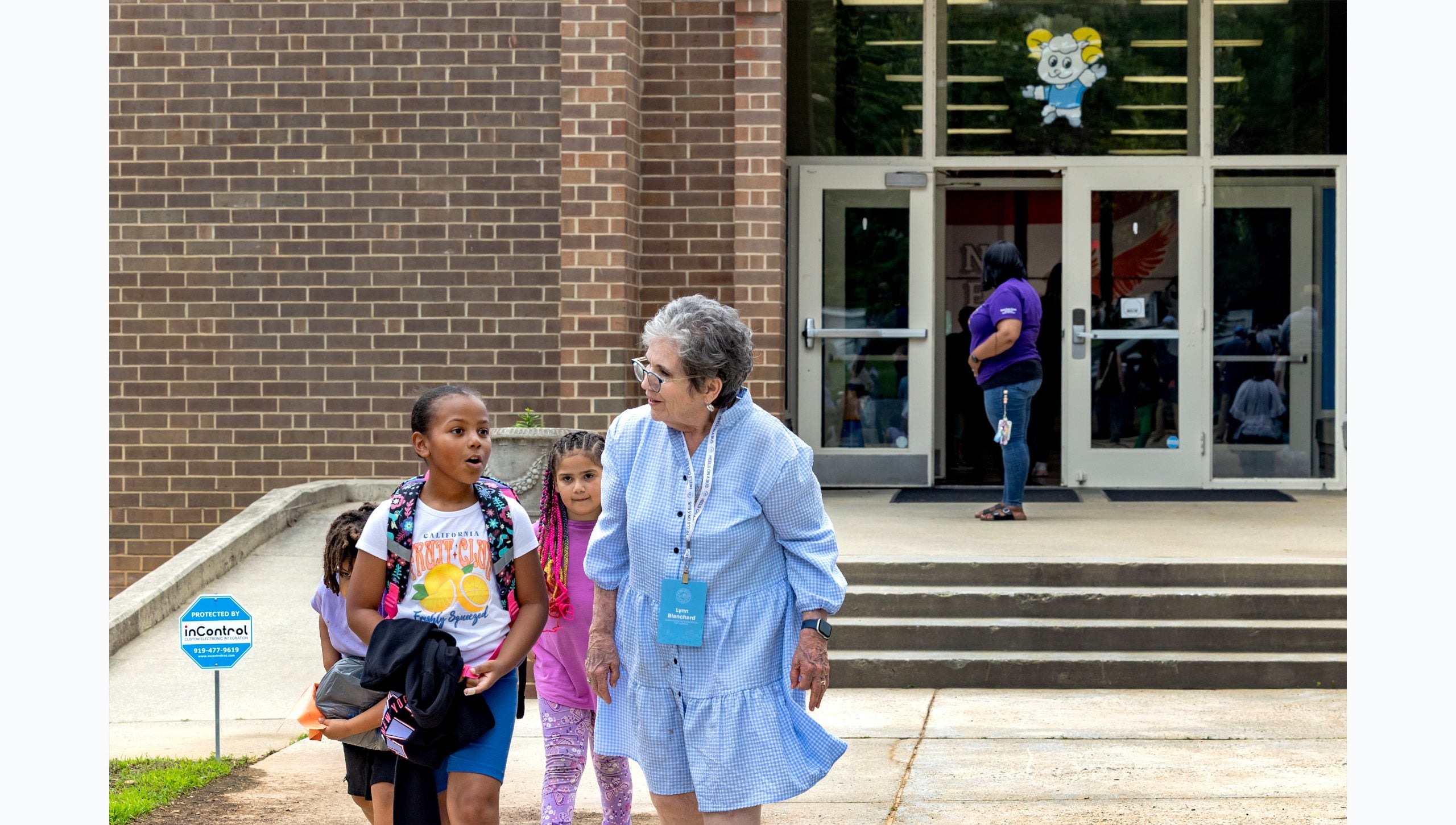 Lynn Blanchard walking with three school children outside Carolina Community Academy in Roxboro.