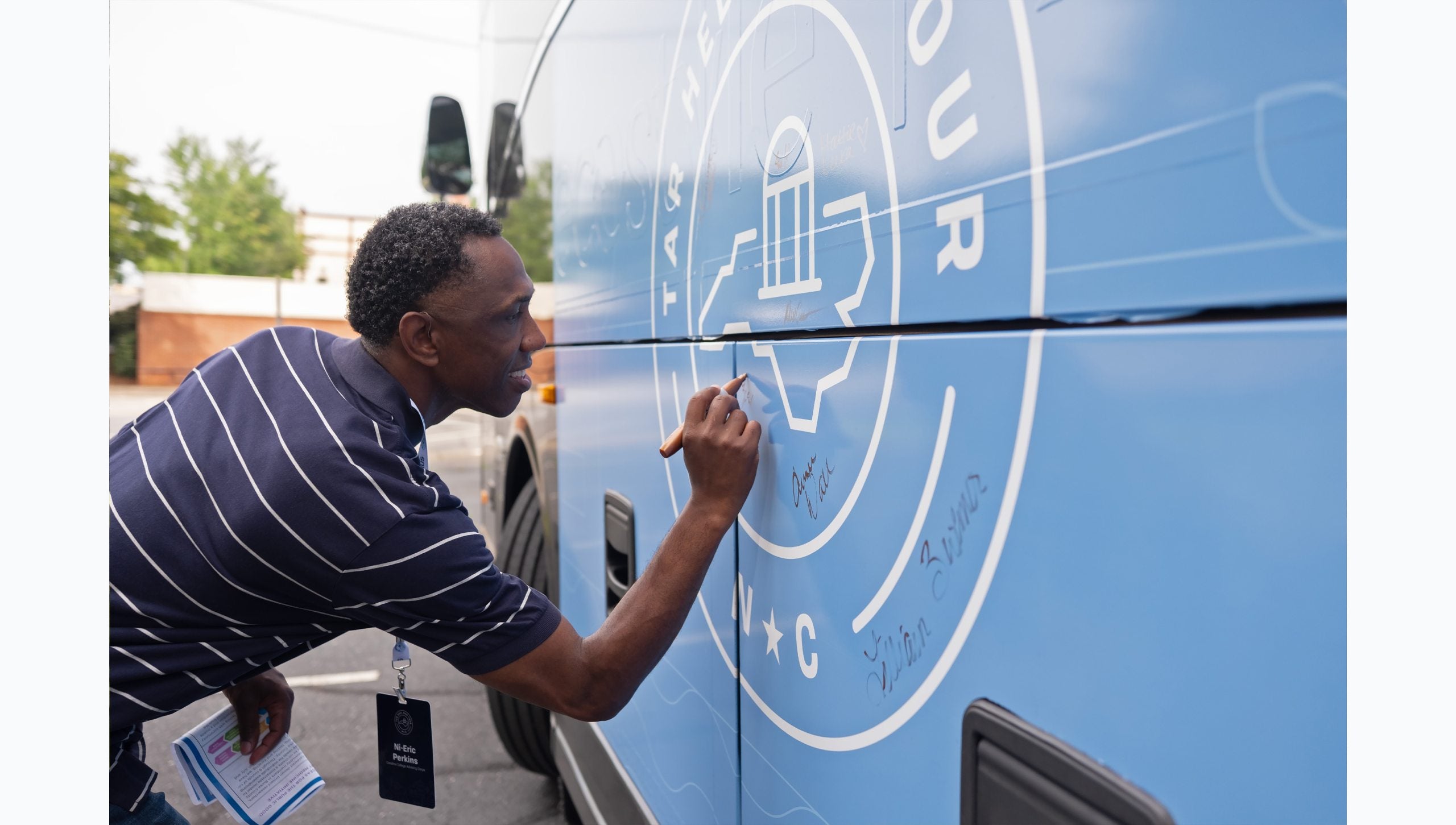 Bus Tour attendee signing the logo on the side of the bus.