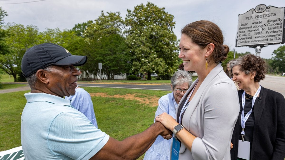Man shaking the hand of a Bus Tour attendee in Warrenton. Seen in the background is a historical marker for the 