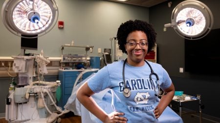 UNC-Chapel Hill nursing student Naomi King posing for a portrait in a hospital room with a Carolina Tar Heels T-shirt on and a stethoscope around her neck.