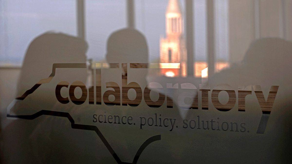 Reflection of Bell Tower at UNC-Chapel Hill seen from a glass window with the silhouette of the N.C. Collaboratory logo.