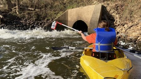 Emily Crawford collecting water specimens while in a canoe.