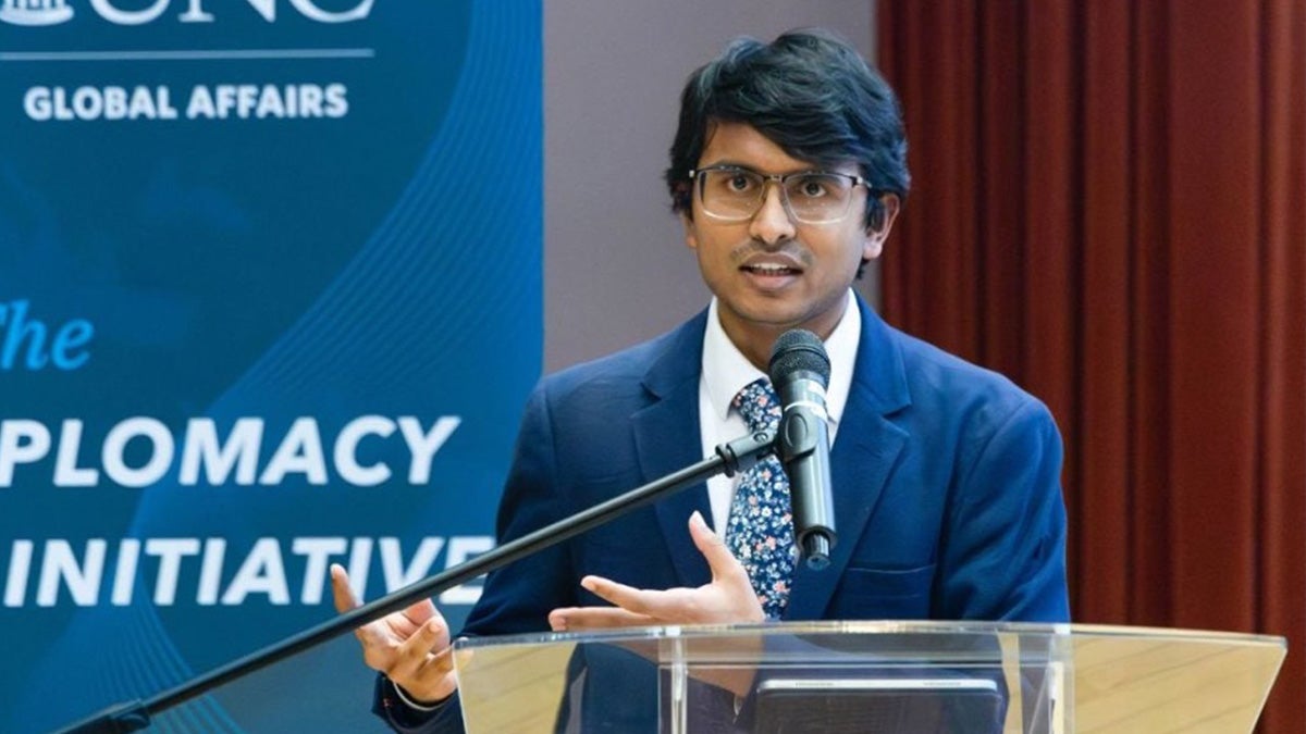 A UNC-Chapel Hill student, Atharv Chakole, speaking into a microphone at a dais at a Diplomacy Initiative event.