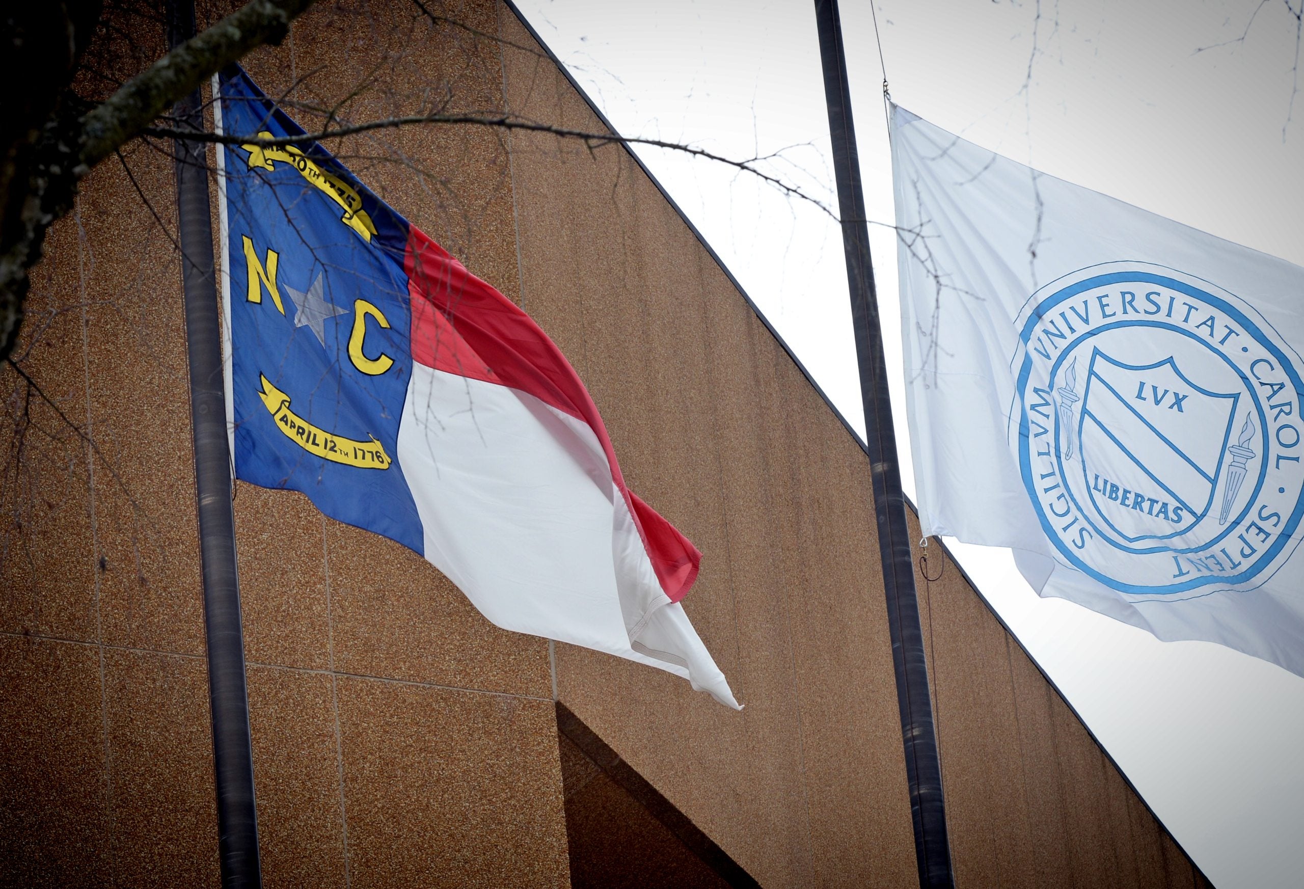 State of North Carolina flag flying next to a flag with the UNC-Chapel Hill seal on it outside the Dean E. Smith Center on the campus of UNC-Chapel Hill.