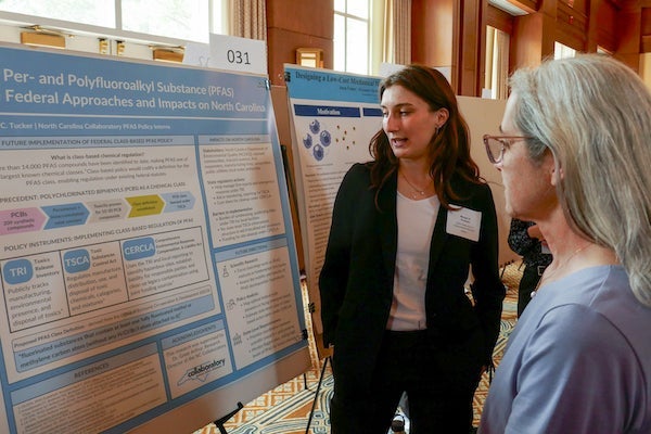 Margot Francini speaking to another woman while standing by a poster board detailing her PFAS research.