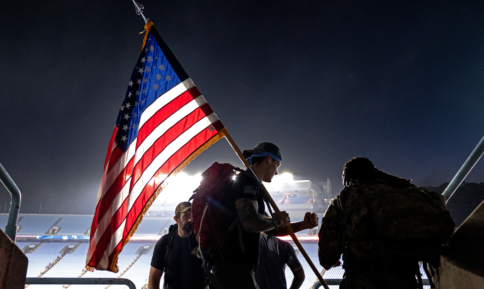 A man holding an American flag with three other people in the background.