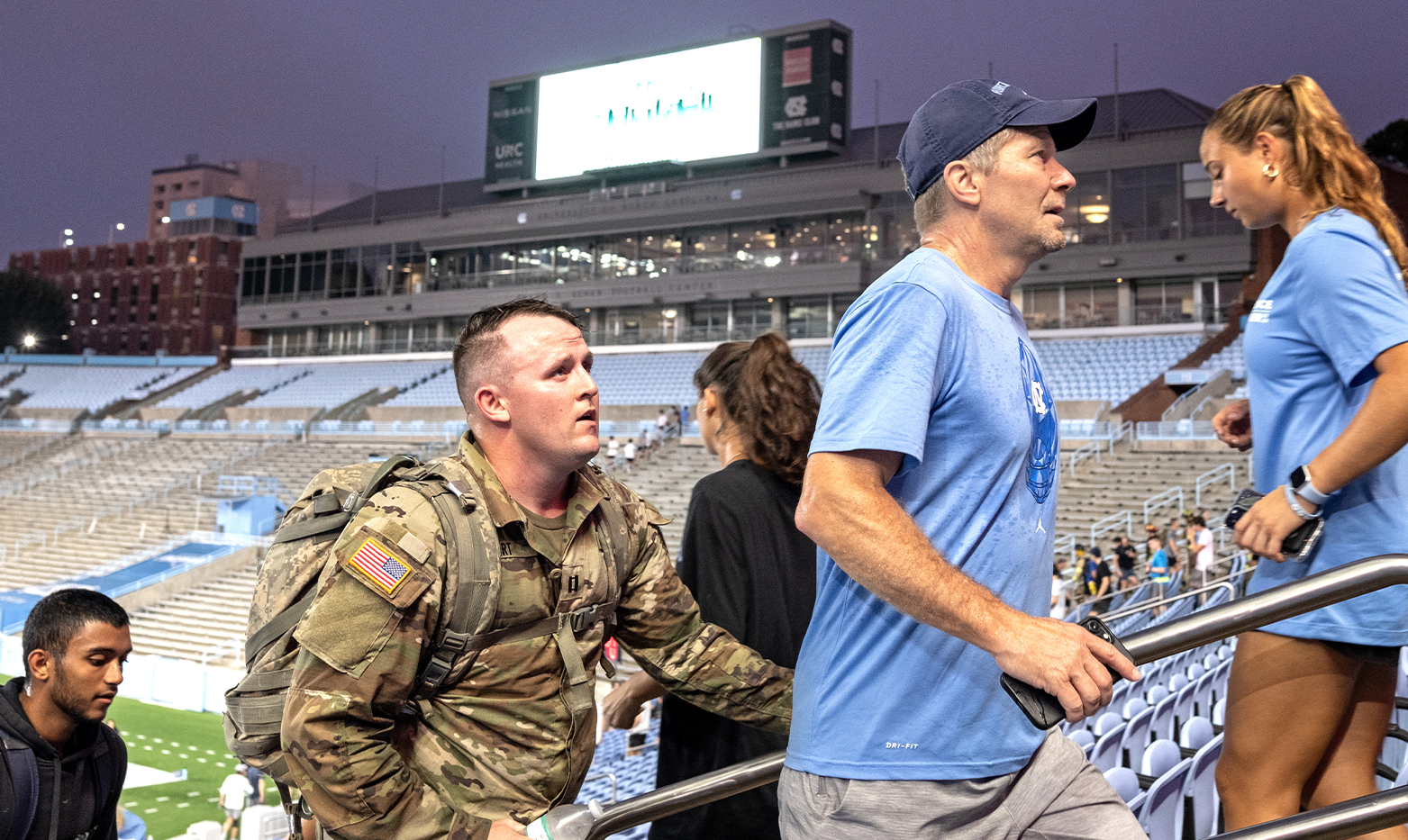 A group of people, including a military member, running up and down stadium steps at dawn.