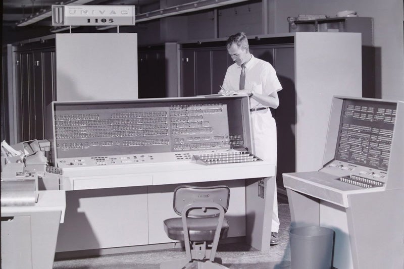 Black-and-white photo of a man in a room-sized computer in the 1950s.