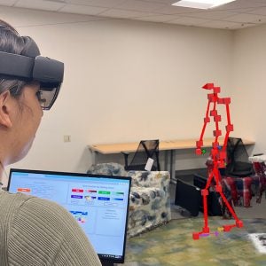 A researcher holding a laptop and wearing a augmented reality glasses as part of research on Parkinson's.